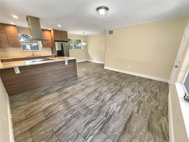 kitchen featuring decorative light fixtures, sink, light stone countertops, wall chimney range hood, and stainless steel fridge