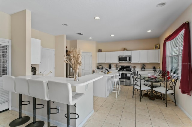 kitchen featuring stainless steel appliances, kitchen peninsula, white cabinets, light tile patterned floors, and a kitchen breakfast bar