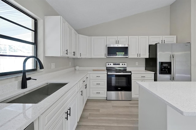 kitchen featuring sink, appliances with stainless steel finishes, lofted ceiling, and white cabinets