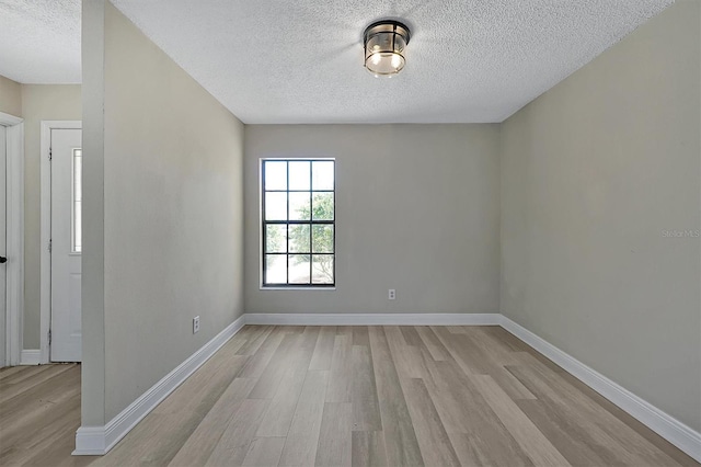 empty room with a textured ceiling and light hardwood / wood-style flooring