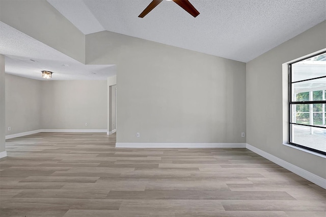 spare room with light wood-type flooring, vaulted ceiling, a textured ceiling, and baseboards