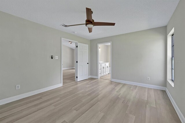 unfurnished bedroom featuring light wood-type flooring, multiple windows, baseboards, and a textured ceiling