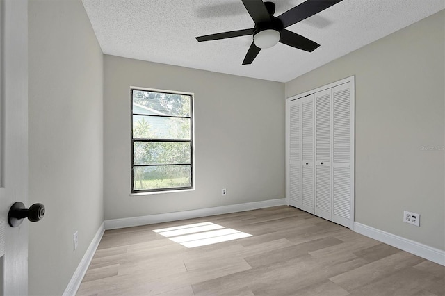 unfurnished bedroom featuring a closet, a textured ceiling, light wood-type flooring, and ceiling fan