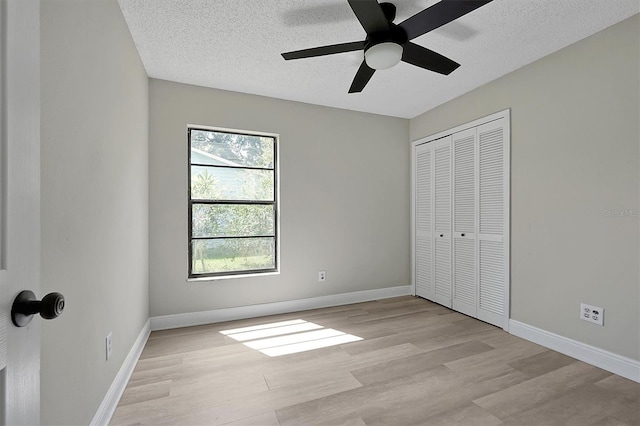 unfurnished bedroom with light wood-type flooring, a closet, a textured ceiling, and baseboards