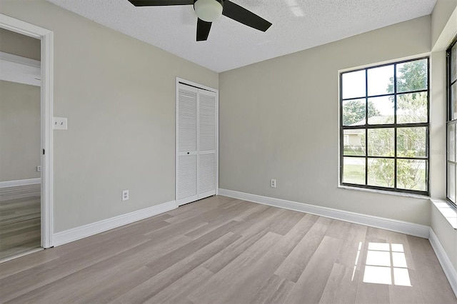 unfurnished bedroom featuring a closet, a textured ceiling, light wood-type flooring, and ceiling fan