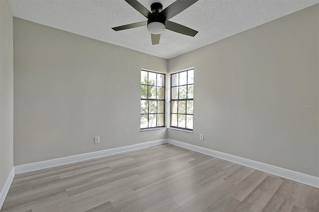 spare room featuring ceiling fan, light wood-style flooring, baseboards, and a textured ceiling