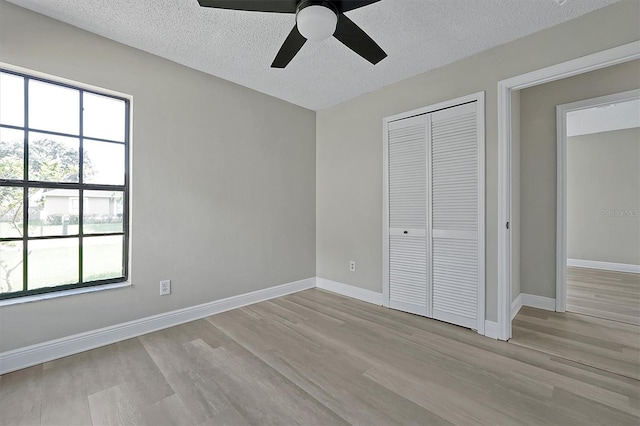 unfurnished bedroom featuring light hardwood / wood-style flooring, multiple windows, a textured ceiling, and ceiling fan