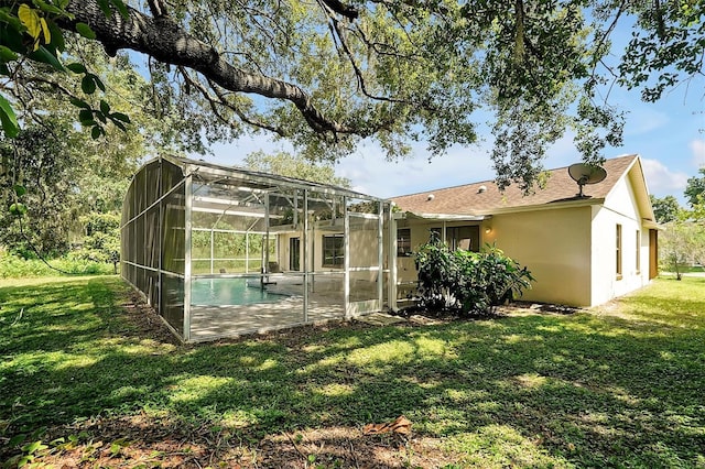 back of property with a yard, glass enclosure, an outdoor pool, and stucco siding