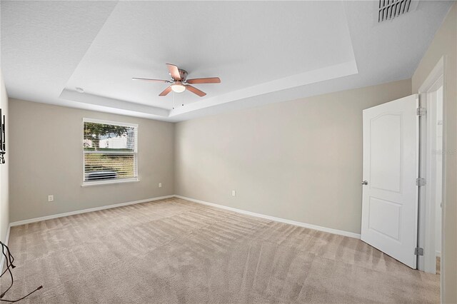 unfurnished room featuring ceiling fan, light carpet, and a tray ceiling