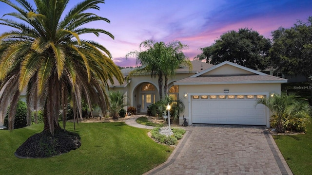 view of front of home featuring decorative driveway, a yard, an attached garage, and stucco siding