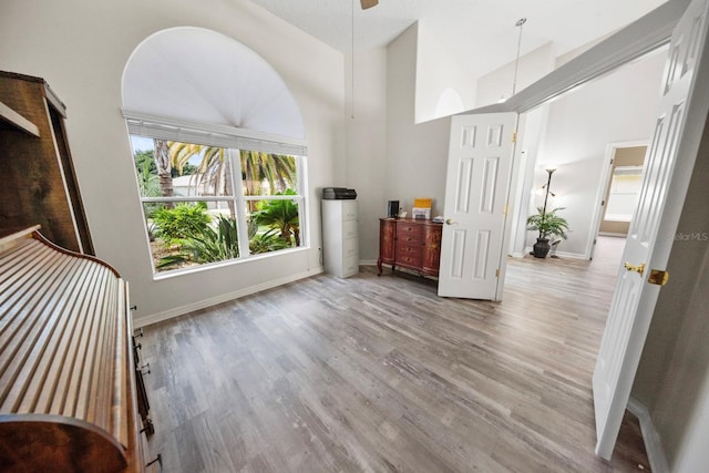 foyer entrance with baseboards, ceiling fan, a towering ceiling, and light wood-style floors