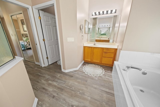 ensuite bathroom featuring baseboards, wood finished floors, ensuite bathroom, vanity, and a bath