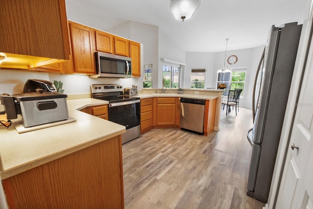 kitchen with light wood-type flooring, a chandelier, hanging light fixtures, kitchen peninsula, and stainless steel appliances