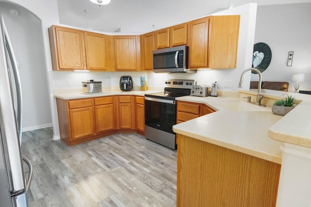 kitchen featuring light wood finished floors, light countertops, appliances with stainless steel finishes, a sink, and a peninsula