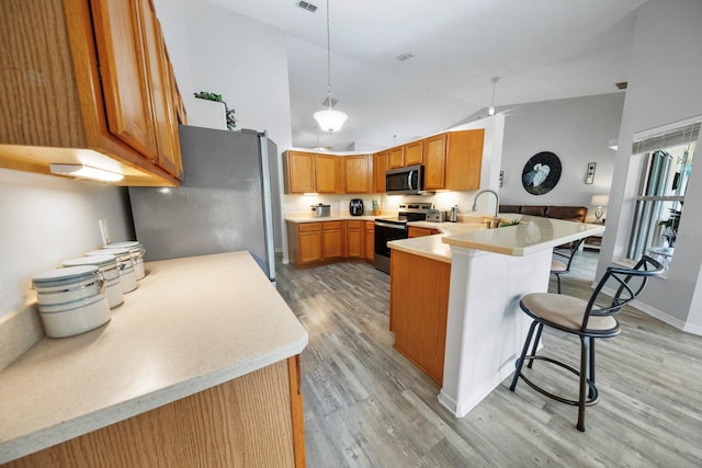 kitchen with pendant lighting, a kitchen bar, light hardwood / wood-style floors, kitchen peninsula, and stainless steel appliances