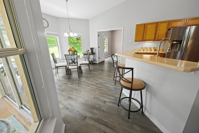 kitchen with stainless steel fridge with ice dispenser, brown cabinets, a kitchen breakfast bar, dark wood-style flooring, and light countertops