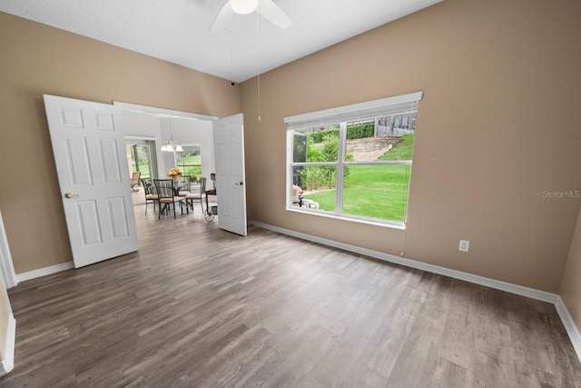 empty room featuring baseboards, wood finished floors, and ceiling fan with notable chandelier