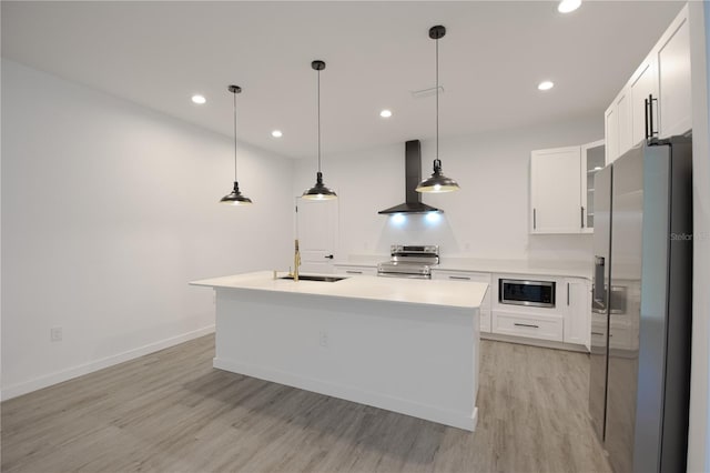 kitchen featuring white cabinets, appliances with stainless steel finishes, sink, wall chimney exhaust hood, and an island with sink