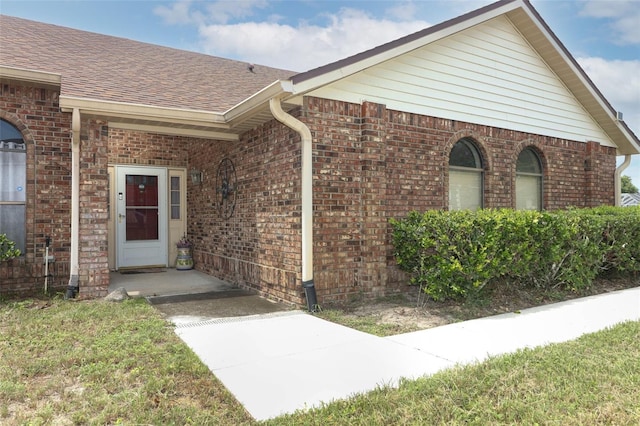 view of exterior entry with brick siding and roof with shingles