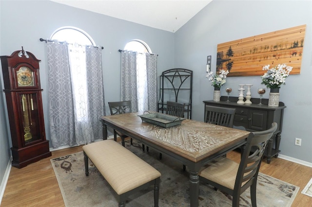 dining room with a healthy amount of sunlight, light wood finished floors, baseboards, and vaulted ceiling