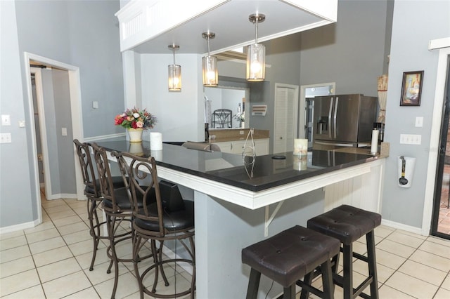 kitchen with light tile patterned flooring, decorative light fixtures, stainless steel fridge with ice dispenser, a breakfast bar area, and kitchen peninsula