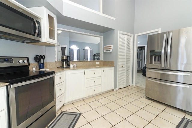 kitchen with white cabinets, light tile patterned floors, light stone countertops, and stainless steel appliances