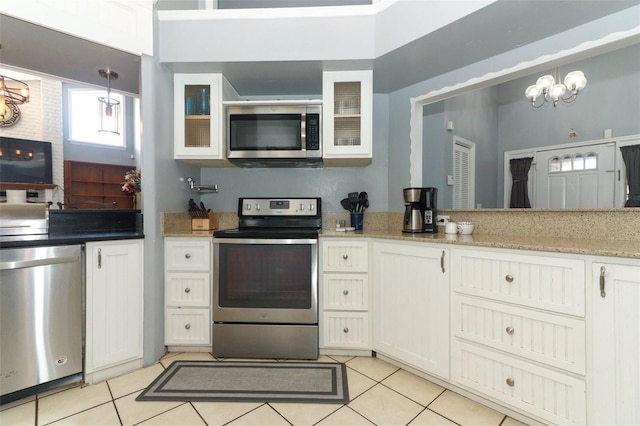 kitchen featuring light tile patterned floors, hanging light fixtures, appliances with stainless steel finishes, glass insert cabinets, and white cabinetry