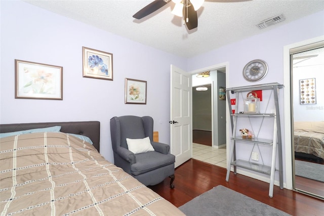 bedroom with ceiling fan, a textured ceiling, visible vents, and wood finished floors