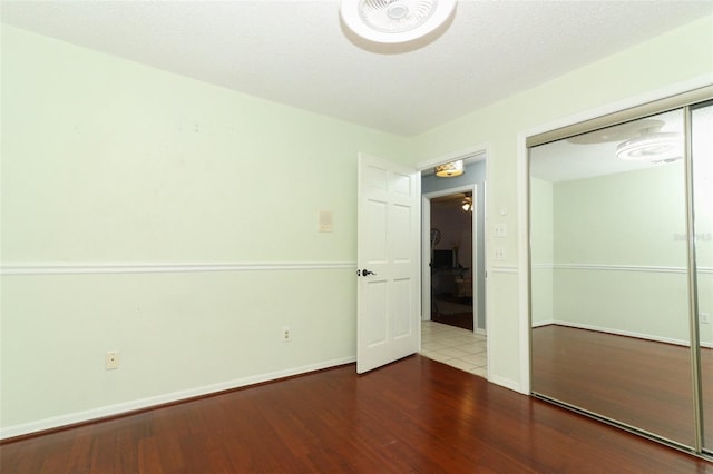 unfurnished bedroom with a textured ceiling, a closet, baseboards, and wood finished floors