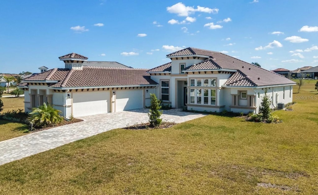 mediterranean / spanish-style house with decorative driveway, a tile roof, stucco siding, an attached garage, and a front lawn