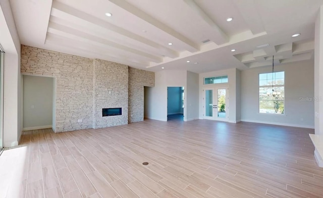 unfurnished living room featuring light wood finished floors, a stone fireplace, beamed ceiling, and baseboards