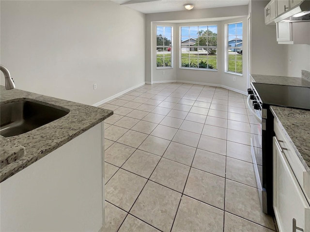 kitchen with range with electric stovetop, light stone countertops, light tile patterned floors, sink, and white cabinetry