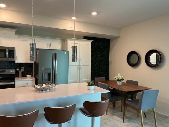 kitchen with white cabinets, backsplash, appliances with stainless steel finishes, pendant lighting, and a kitchen bar