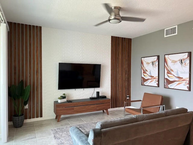 living room featuring light tile patterned floors, ceiling fan, visible vents, and a textured ceiling