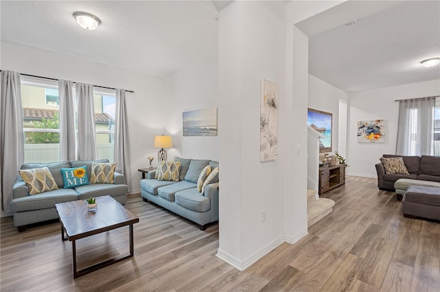 living room featuring light wood-style floors, plenty of natural light, a textured ceiling, and baseboards