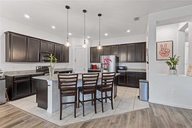 kitchen featuring decorative light fixtures, a breakfast bar area, appliances with stainless steel finishes, light wood-style floors, and dark brown cabinetry