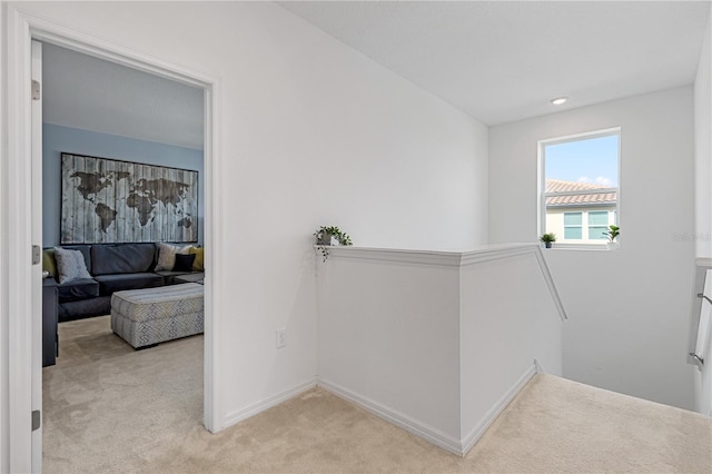 corridor featuring an upstairs landing, light colored carpet, and baseboards