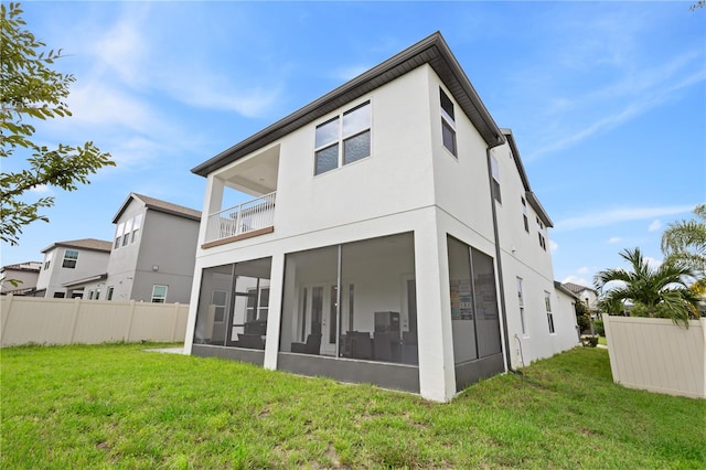 rear view of property featuring a yard, a sunroom, fence, and stucco siding