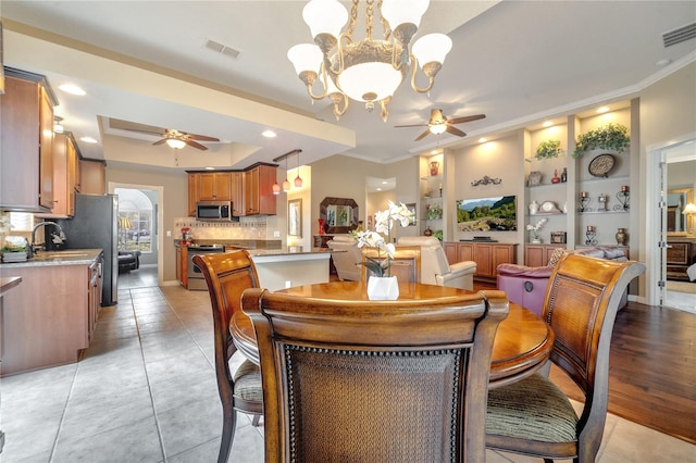 dining room with light hardwood / wood-style floors, sink, crown molding, a raised ceiling, and ceiling fan with notable chandelier