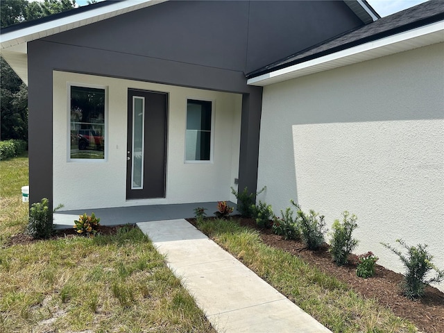 view of exterior entry with a yard and stucco siding