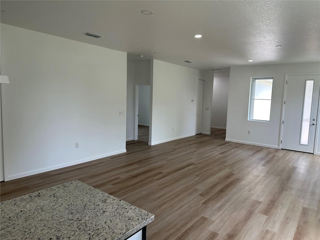 unfurnished living room featuring visible vents, baseboards, light wood-style flooring, a textured ceiling, and recessed lighting