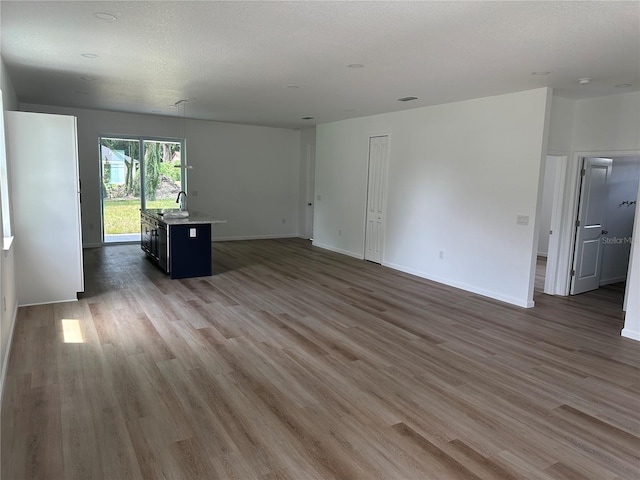 unfurnished living room featuring a textured ceiling, dark wood-style flooring, a sink, and baseboards