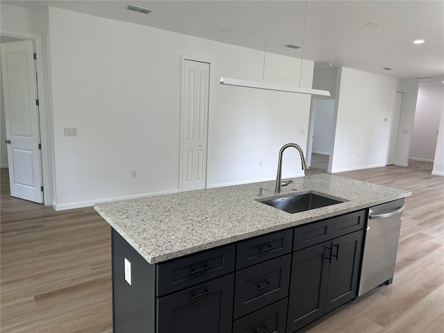 kitchen with light stone counters, a kitchen island with sink, a sink, light wood-style floors, and dishwasher