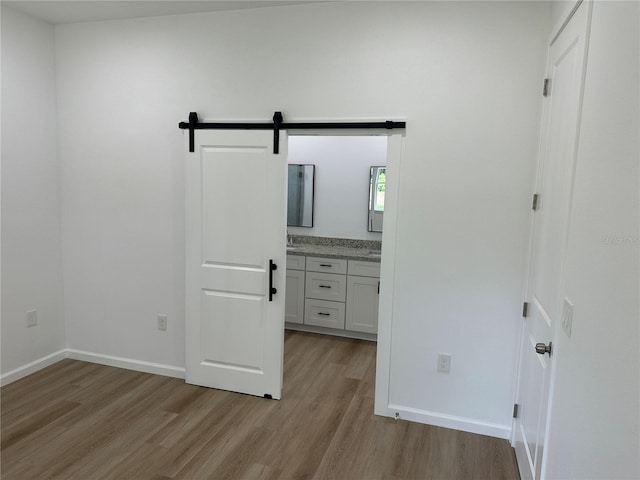 unfurnished bedroom with a barn door, connected bathroom, light wood-style flooring, and baseboards