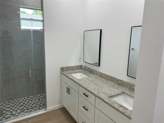 bathroom featuring double vanity, a stall shower, a sink, and wood finished floors