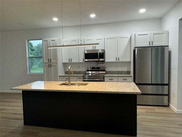 kitchen featuring appliances with stainless steel finishes, white cabinets, a sink, and an island with sink