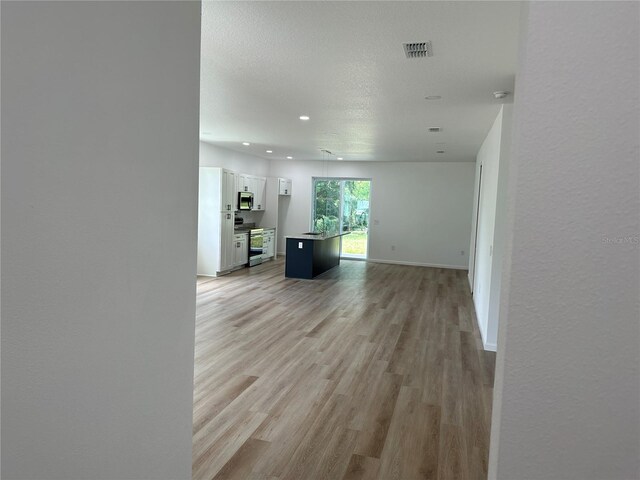 interior space with a textured ceiling, recessed lighting, visible vents, baseboards, and light wood finished floors