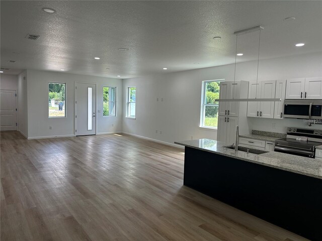 kitchen featuring a sink, white cabinets, appliances with stainless steel finishes, light stone countertops, and pendant lighting