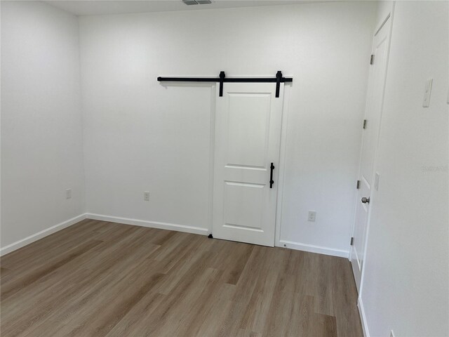 spare room with light wood-type flooring, baseboards, visible vents, and a barn door