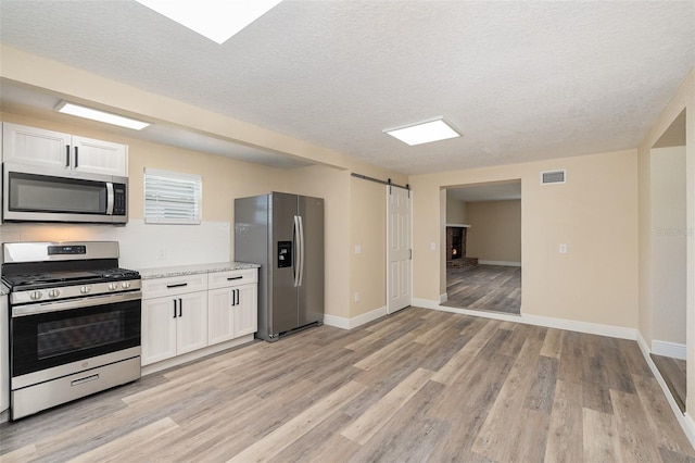 kitchen with white cabinetry, a barn door, a textured ceiling, appliances with stainless steel finishes, and light wood-type flooring